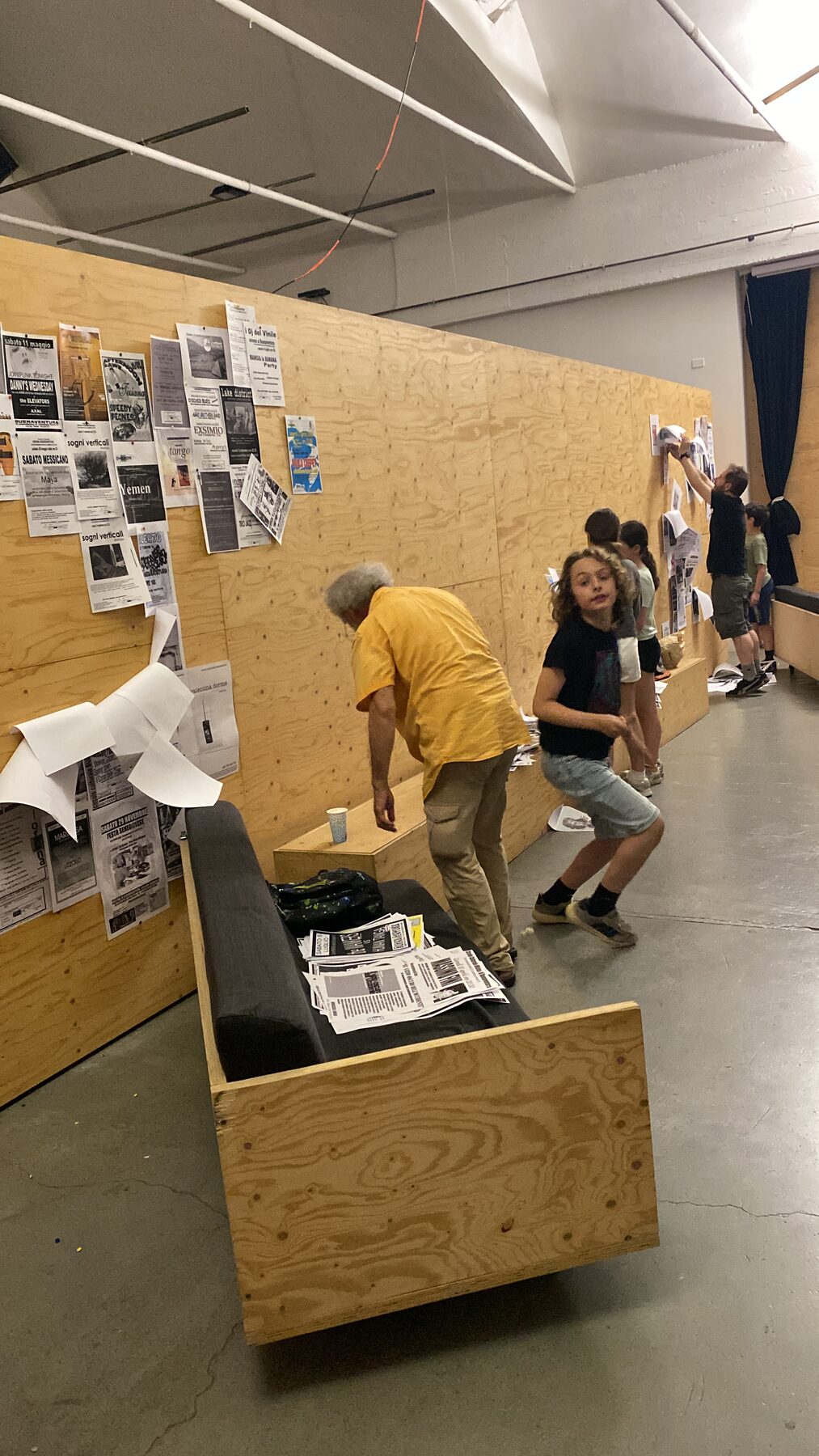 Persone sedute per terra che sfogliano i vecchi flyer e poster del Buena 1.0 disposti sul pavimento di legno