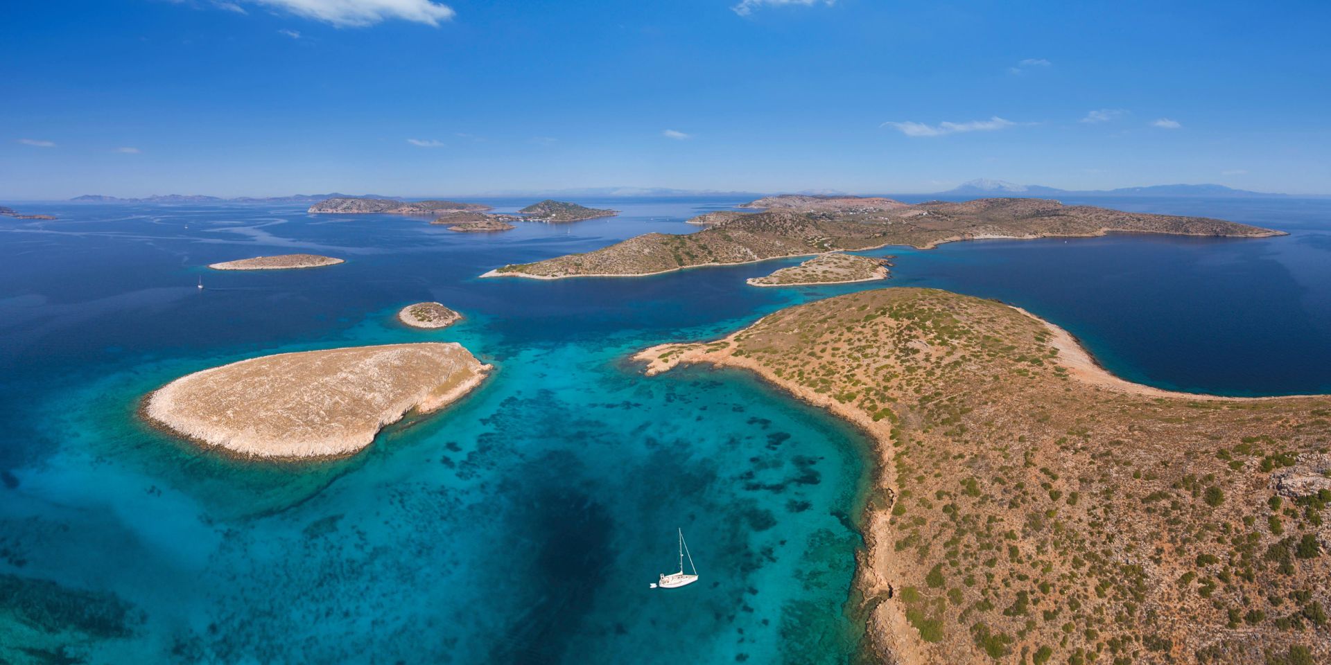 Vista aerea dell'arcipelago di Arki nel Dodecaneso. Acqua turchese, isolotti bassi e brulli, una barchetta a vela all'ancora nel mezzo della baia.